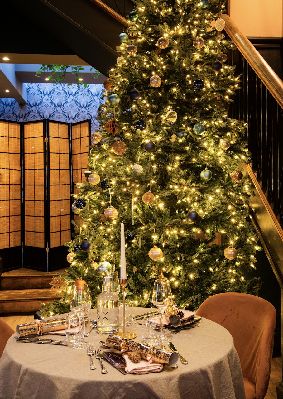 Table for two set with crackers and candles beneath the lit Christmas tree at SIX
