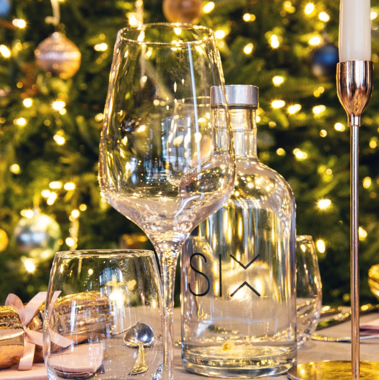 SIX glassware and a candlestick in front of a softly lit Christmas tree