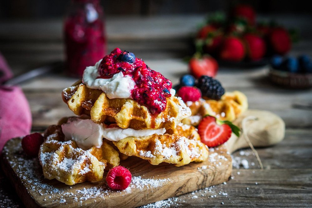 Organic waffles with cream and fresh berries on a wooden board