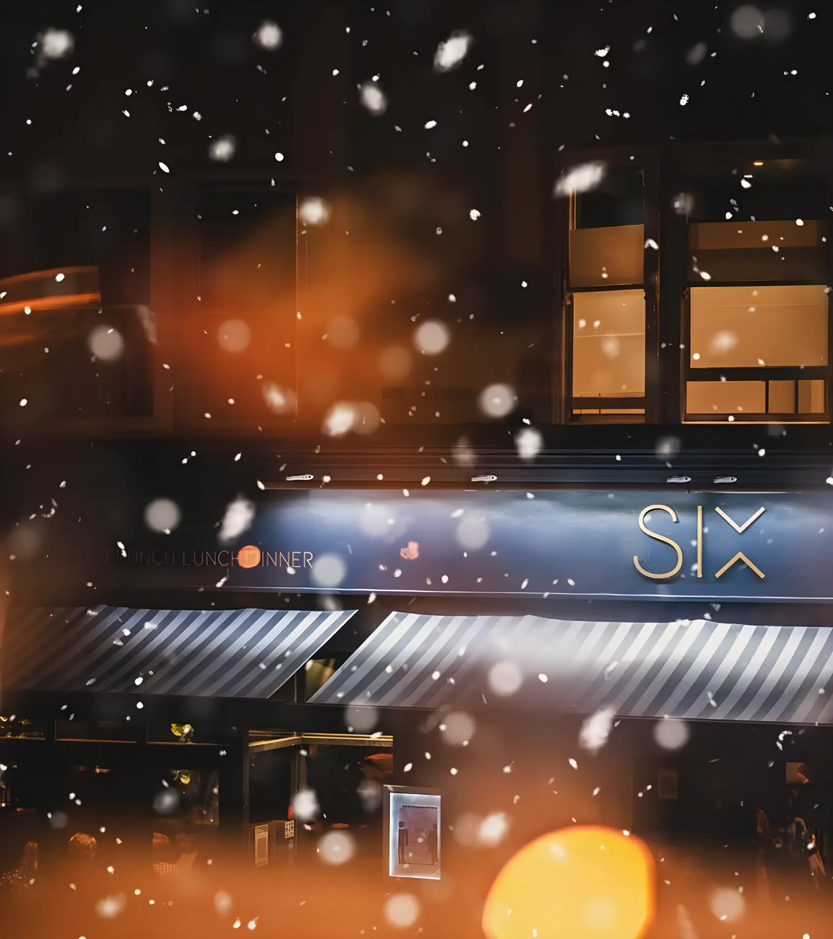 Snow falling past the lit SIX sign on Western Road at night